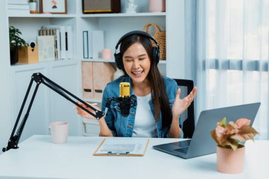 Sosyal medyada kulaklıkla canlı yayın yapan Asyalı sunucu modern stüdyoda yaşam koçluğu veya pazarlama dinleyicilerini selamlıyor. Taktik.