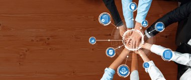This image showcases a diverse group of hands coming together on a wooden desk, symbolizing collaboration and teamwork in a business environment, enhanced by technology icons. Amity