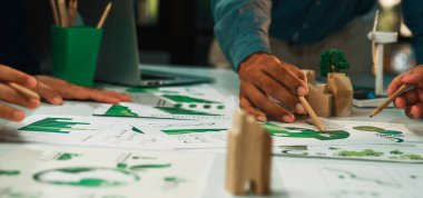 Bu görüntü, sürdürülebilir kalkınma odaklı, çevre dostu tasarım modelleri ve grafikleri sergileyen işbirlikçi bir planlama oturumuna katılan dinamik bir ekip yakalar. SACTR