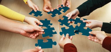 Çeşitli bir grup el, parlak, ahşap bir masa üzerinde, takım çalışması, işbirliği ve neşe dolu parçaları bir araya getirmek için uzanır. SACTR