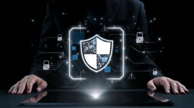 Siyah takım elbiseli profesyonel bir adam dijital elementlerle çevrili siber güvenlikle meşgul. Kalkan grafiği veri korumasını ve çevrimiçi güvenlik önlemlerini sembolize eder. Dörtgen