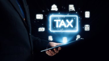 Bir işadamı, modern iş uygulamaları ve vergi idaresinde finans ve teknolojinin kesişimini gösteren, parlayan vergi simgelerini gösteren bir tablet tutuyor. Dörtgen