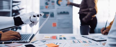 Gelecekçi bir robotik el dizüstü bilgisayar kullanırken bir işletme ekibi şık bir ofis ortamında grafikler ve grafikler üzerinde tartışıyor ve işbirliği sergiliyor.