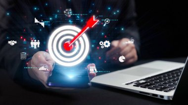 Dijital grafiklerle çevrili, iş stratejisi ve yenilikleri temsil eden parlak bir hedef simgesiyle akıllı bir telefonu tutan resimli bir sahne. Dörtgen