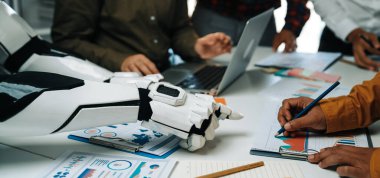 Modern ofis ortamında, bir robot kolu verileri analiz etmek, yenilikçi stratejiler gösteren çizelgeler ve belgeler sunmak üzere toplantı sırasında insan katılımcılarla işbirliği yapar.