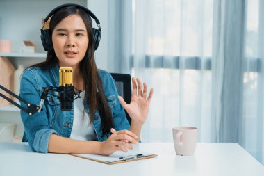 Sosyal medyada kulaklıkla canlı yayın yapan Asyalı sunucu modern stüdyoda yaşam koçluğu veya pazarlama dinleyicilerini selamlıyor. Taktik.