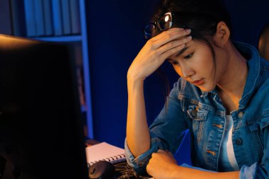 Stresli, genç, güzel Asyalı yaratıcı proje yaratıcısı sosyal medyayı araştırmak için bilgisayara bakıyor ve geceleri daha çok neon modern ofisin planlama kanalı stratejisine ulaşılıyor. Taktik.