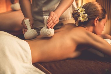 Sıcak bitkisel top spa masaj vücut tedavisi, masör nazikçe bitki torbasını çift müşteri vücuduna bastırıyor. Aromaterapi salonda mumların sıcacık ışığında dinlenme sükuneti. Sessiz.