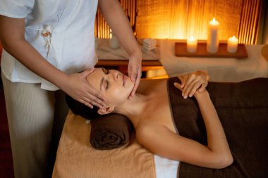 Beyaz kadın stres önleyici kafa masajı yapmaktan ve lüks otel veya otelde sıcak mum ışığında yüz güzelliği eğlencesi yapmaktan zevk alıyor. Sessiz.