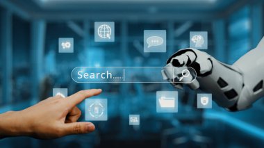 Bu resim, modern bir ofiste, insan ve yapay zeka arasındaki etkileşimi sembolize eden bir robot elin yanında dijital bir arama çubuğuna dokunan bir insan elini gösteriyor. Auvana