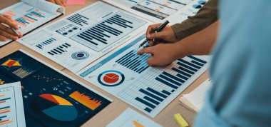 Bir grup profesyonel, gelecekteki projeler ve performans değerlendirmesi için canlı tartışmalar ve stratejik planlama ile ilgilenen çeşitli iş haritaları ve grafikleri üzerinde işbirliği yapmaktadır. SACTR