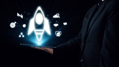 Bir işadamı, teknolojinin dijital çağında yenilik, büyüme ve girişimci ruhu sembolize eden, gelecekteki roket simgelerini gösteren bir tablet sunuyor. Dörtgen