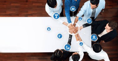 A dynamic scene of teamwork, showcasing diverse individuals joining their hands in unity around a white table with icons representing business success and collaboration. Amity