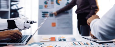 İş toplantısına katılan, verileri analiz eden ve profesyonel bir ortamda insan takımıyla işbirliği yapan modern bir ofis sahnesi. Noogenesis