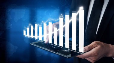 A businessman engages with a tablet displaying financial growth through vibrant digital graphs, highlighting the intersection of technology and business analytics. Copula