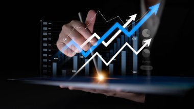 A businessman holds a tablet displaying a financial graph with an upward trend, showcasing data analytics and market growth against a dark background. Scalp