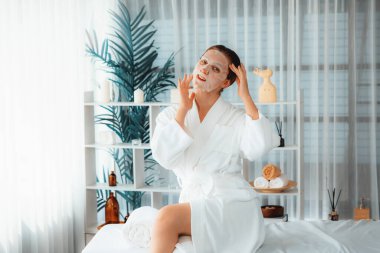 Kaplıca salonunun sakin, modern gün ışığı atmosferi, kadın müşteri poz veriyor ve yüz maskesi ile gençleştiriyor. Yüz bakımı ve güzellik kozmetolojisi prosedürü. Sessiz.