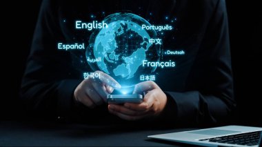 Bu resim, çeşitli dilleri gösteren bir akıllı telefon ile modern küresel iletişim kavramını gösteriyor. Kültürleri birbirine bağlayan teknolojinin önemini vurguluyor. Dörtgen