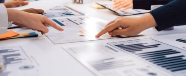 Çeşitli profesyonellerden oluşan bir grup, bir toplantı sırasında iş haritaları ve grafikleri analiz ederek modern bir ofiste işbirliği yapıyor. Sahne, takım çalışması ve iletişimi ön plana çıkarıyor. SACTR