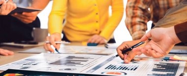 Çeşitli bir iş ekibi, modern bir ofis masasında piyasa raporlarını ve finansal grafikleri inceleyerek takım çalışması ve üretkenlik sergiledi. SACTR