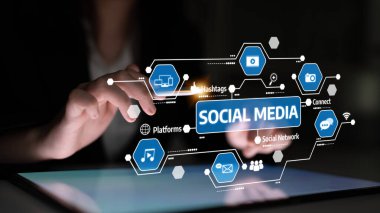 Bir kişi, çeşitli sosyal medya simgeleri ve hashtag 'lerini gösteren bir tabletle etkileşime girerek, dijital iletişimin ve bağlanabilirliğin gelişen manzarasını resmediyor. Tessel