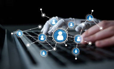 İnsan-makine etkileşiminin geleceğini gösteren, kullanıcı bağlantılarını ve teknolojisini sembolize eden dijital simgelerle çevrili bir dizüstü bilgisayarın klavyesine yazı yazan robot elin yakın çekimi. Tessel