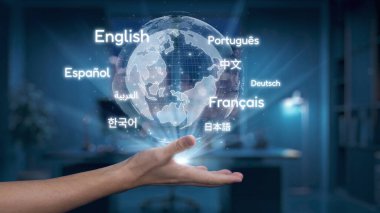 Bir el, modern ofis ortamında küresel iletişimin ve çeşitliliğin özünü sembolize eden dilleri gösteren parlayan bir küreyi tutuyor. Auvana