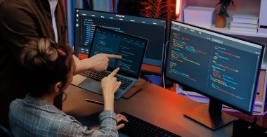 Modern ofisteki neon ışık odasında bilgi ağını gösteren dizüstü bilgisayarla iki ekranda veri çalıştıran akıllı web sitesi geliştirme kodlayıcı sistemini tartışan IT geliştiricilerinin ciddiyeti. İnfobahn.