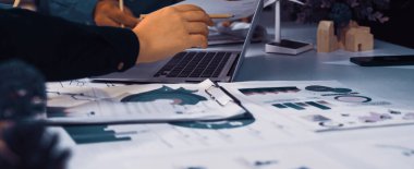 Modern bir ofis sahnesinde sürdürülebilirlik ve yeşil çözümler, belgeler, bir dizüstü bilgisayar ve aktif olarak tartışılan eller üzerinde odaklanmış bir ortak toplantı yer alıyor. SACTR