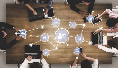 A top-down view of a collaborative workspace featuring diverse individuals engaged with technology like laptops and tablets, surrounded by digital connectivity elements. Tessel