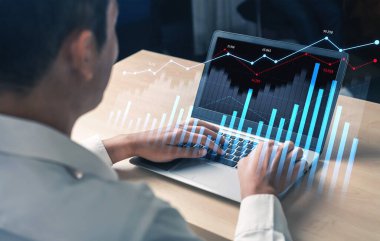 Profesyonel bir ortamda piyasa performans sezgilerini geliştirmek için dizüstü bilgisayar, finansal grafikler ve istatistikler kullanan bir kişi. Kafa derisi