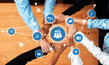 Bir iş ortamında iletişim ve medya paylaşımını temsil eden teknoloji ikonlarıyla çevrili bir masanın üzerinde çeşitli ellerin yer aldığı takım çalışması ve işbirliğini vurgulayan dinamik bir sahne. Dostluk