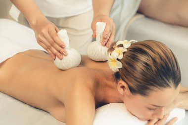 Sıcak bitkisel top spa masaj vücut tedavisi, masör nazikçe bitki torbasını çift müşteri vücuduna bastırıyor. Aromaterapi dinlenme sükuneti ve sükuneti kaplıca salonundaki atmosferi aydınlatıyor. Sessiz.