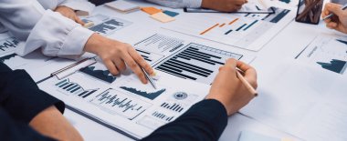 Çeşitli profesyonellerden oluşan bir grup, iş raporları ve veri eğilimlerini analiz eden bir işbirliği oturumunda yer alıyor. Çeşitli grafikler ve grafikler anahtar performans göstergelerini vurguluyor. SACTR