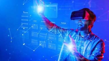 Dijital arayüz ve mavi görsellerle çevrili bir sanal gerçeklik kulaklığı ile coşkuyla etkileşime giren bir kişi, gelişmekte olan teknoloji ve yeniliğin heyecanını sergiliyor. Raster.