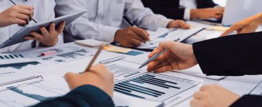 Çeşitli bir ekip, etkin bir büyüme için stratejik planlama ve performans analizine odaklanarak, grafikler ve dijital cihazlarla çevrili işbirlikçi bir iş toplantısı düzenliyor. SACTR