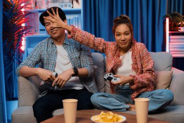 Oyun oynayan mutlu çiftin oturduğu kanepe joystickle oyun oynuyordu. Önden atıştırmalıklar ve kazanmak için gözlerini kapayan içkiler, evdeki modern neon ışıklı oturma odasında eğlenceli bir şekilde meydan okumaydı. İnfobahn.