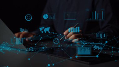 Bir işadamı dijital tabloları ve grafikleri gösterilen bir dizüstü bilgisayarla veri eğilimlerine odaklanarak, modern bir ofiste bilgilendirilmiş mali karar alma mekanizmasının iç yüzünü vurguluyor. Xenic