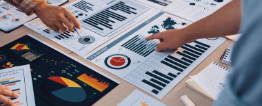 Çeşitli bir iş ekibi toplantı sırasında veri analizi yapar. Modern ofis ortamında bilinçli stratejik kararlar almak için grafikler ve çizelgeler keşfediyorlar. SACTR