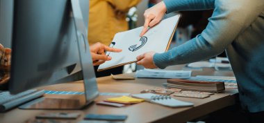 A dynamic workspace showcases team members exchanging ideas over a sketch on a clipboard, with a digital screen in a collaborative office setting. SACTR