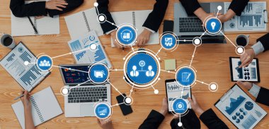 Bir grup iş adamı, veri görselleştirme ve grafiklerle çevrili dizüstü bilgisayarlar ve tabletler kullanarak stratejik tartışmaları teşvik ederek ortak bir toplantıya katıldı. Dostluk