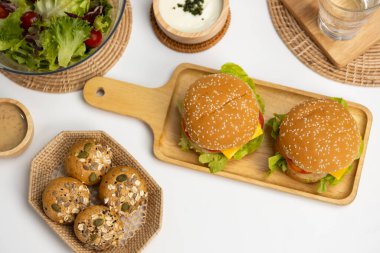 Çifte köfteli hamburger, salata, beyaz masa arkasında ev yapımı servis edilen yemeğin kepekli çöreği. Restoran ya da kafe menüleri hazırlanıyor. İnfobahn.