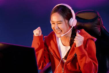Yüzünde kulaklık renginde kulaklık takan, neon odada online oyun oynayan, Esport meziyetli takım oyuncularına yumruk kaldırarak oynayan güzel Asyalı kız flamasının sunucu kanalı. Taktik.