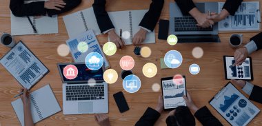 Çeşitli bir iş ekibi, yenilik ve takım çalışmasını gösteren grafikler ve teknolojiyle dolu bir masa etrafında işbirlikçi strateji planlamasına girişiyor. Çapraz