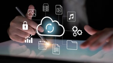 Bir işadamı bulut depolama simgelerini gösteren bir tabletle etkileşime girerek, modern teknoloji ve iş çözümleri için veri senkronizasyonu, güvenlik ve yönetimi vurguluyor. Gantry