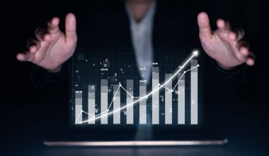 Bir işadamı, karanlık bir ortamda gelecekteki iş gelişimine ilişkin finansal başarıyı ve yenilikçi stratejileri simgeleyen bir dijital büyüme tablosunu dizüstü bilgisayarında sergiliyor. Etki