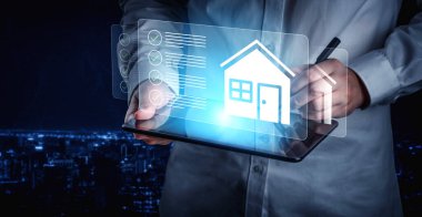 Bir profesyonel dijital tabletle ilgilenir, gelecekçi bir şehir manzarasına karşı bir ev tasarımı projesi çizer, teknoloji ve yaratıcı planlamanın kesişimini gösterir. Gantry