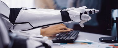 Modern ofis ortamında bilgisayar klavyesiyle etkileşime giren robotik bir kolun yakın çekimi, iş yerindeki teknoloji ve insan çalışmalarının karışımını vurguluyor. Noogenesis