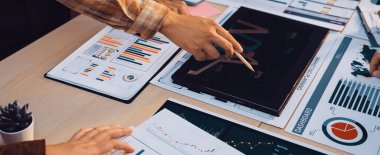 Belgeler ve çizelgeler üzerindeki mali verilerin analiz edildiği ortak bir iş toplantısı. Profesyonel bir ortamda takım çalışması ve stratejik karar verme üzerinde duruluyor. SACTR