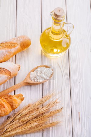 Foto de Composición espigas de centeno croissant baguettes harina en cuchara botella aceite sobre tablas blancas concepto de alimentos y bebidas - Imagen libre de derechos